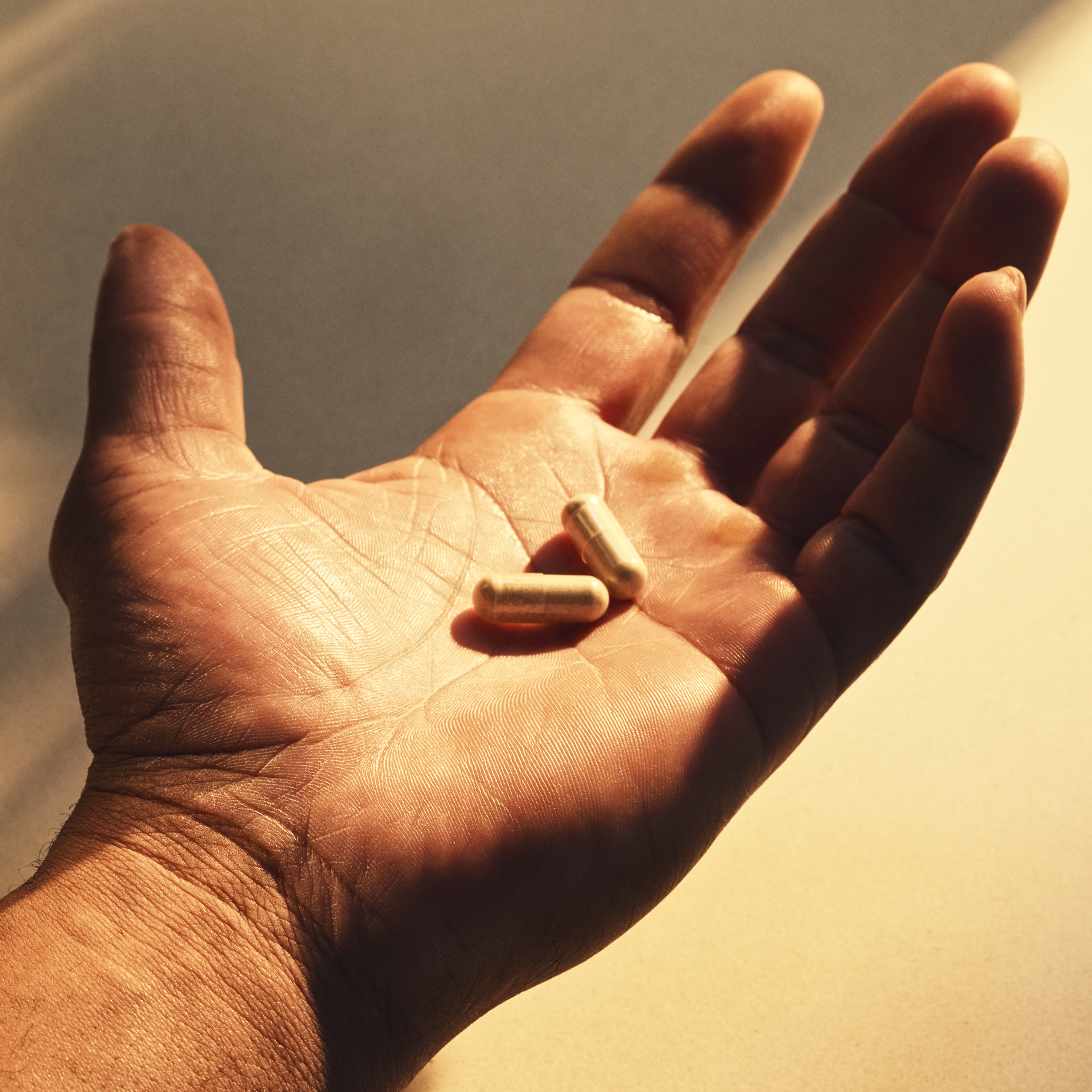 Single tan capsule resting in an open palm against a neutral background.