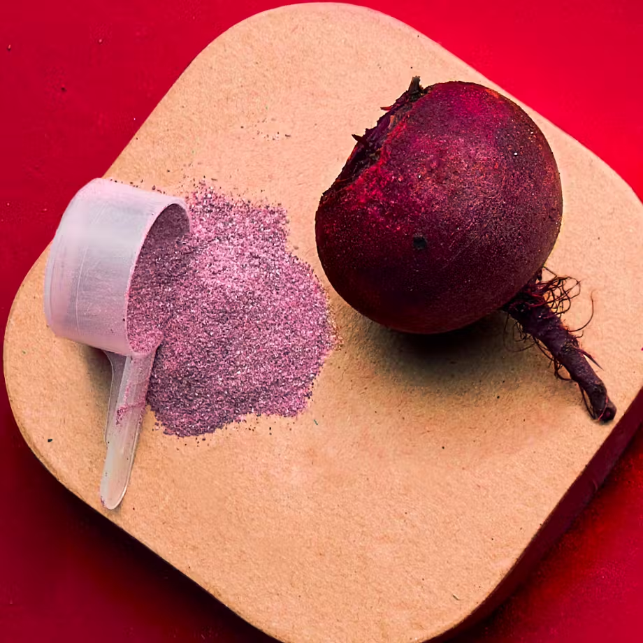 Beetroot next to a scoop of pink powder on a beige surface with a red background